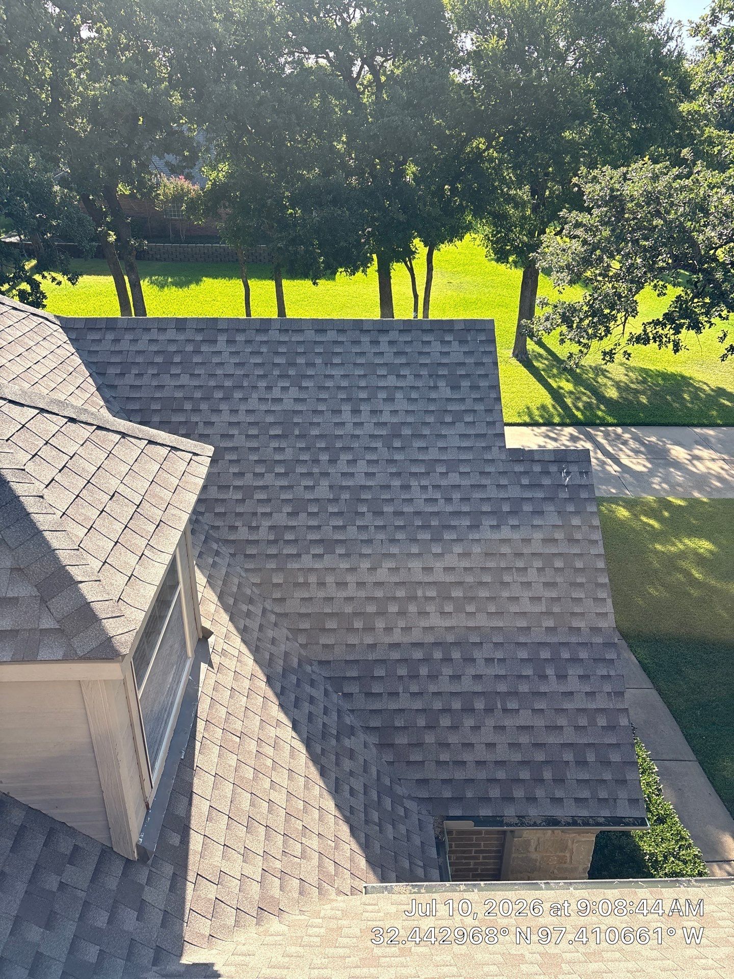 Gabled gray shingle rooftops beside a sunlit green yard with trees and a stone path.