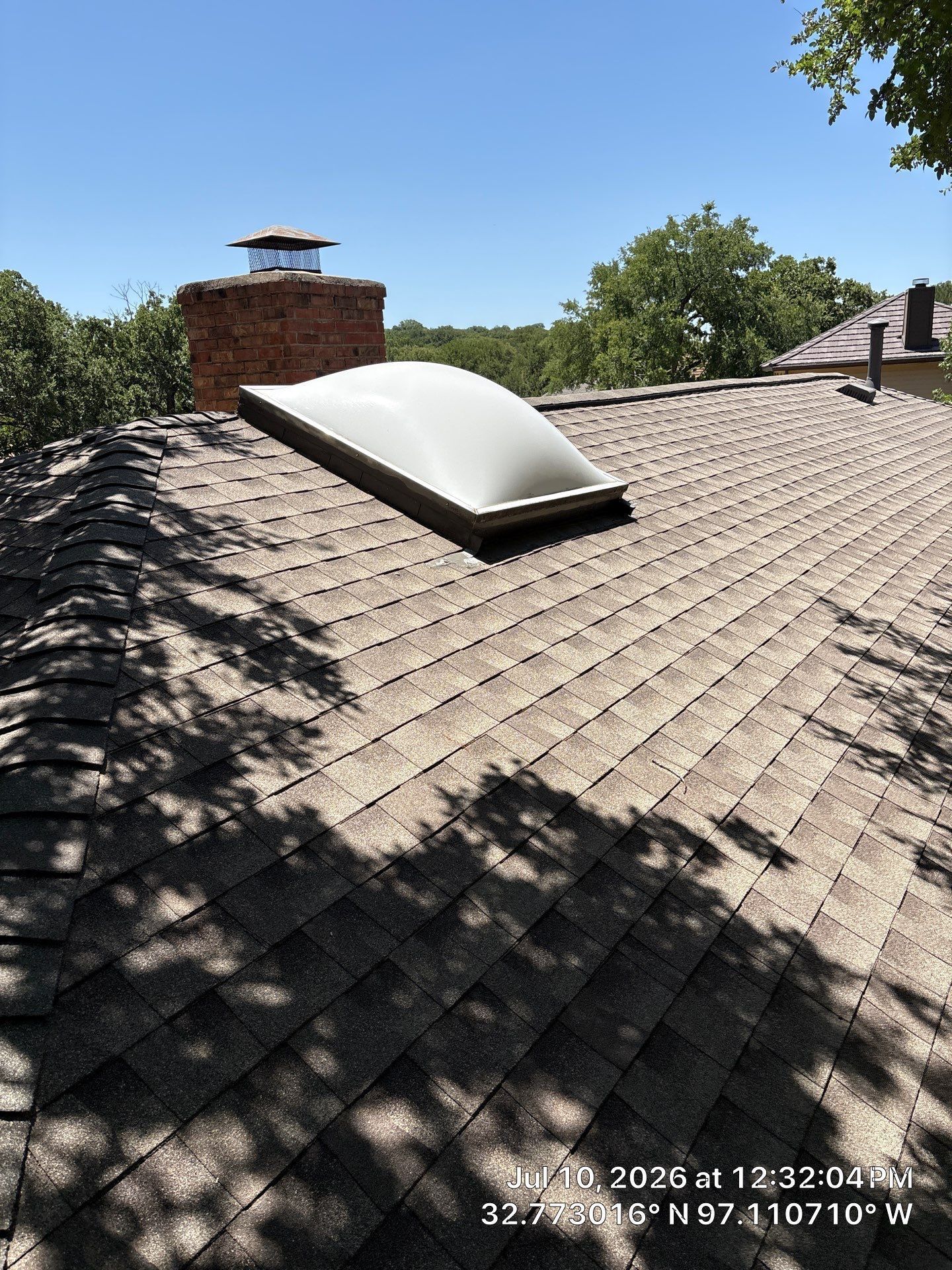 Rooftop with a white skylight dome on gray shingles under a clear blue sky.