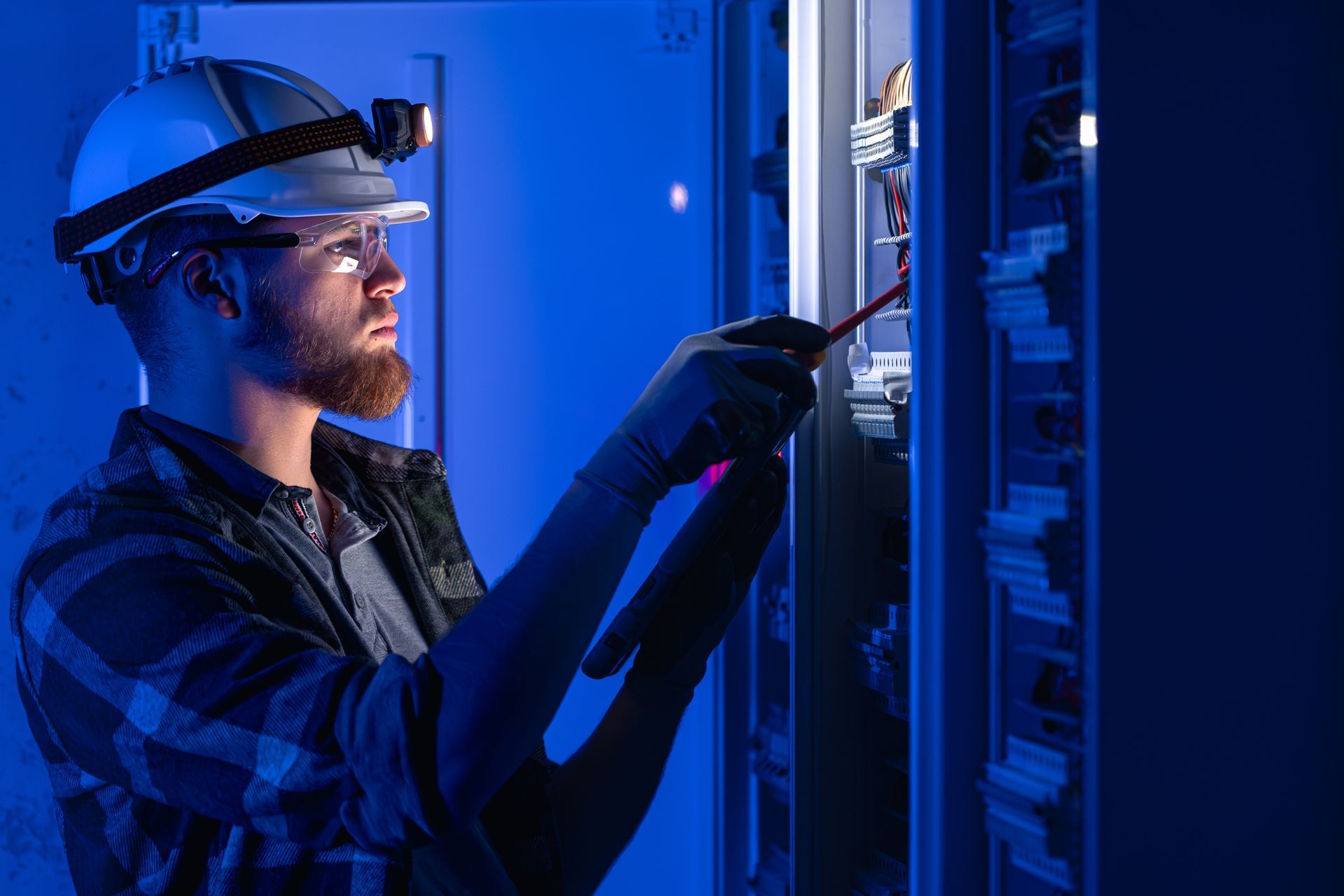 Technician in blue light adjusting server rack cables while wearing a headlamp and gloves