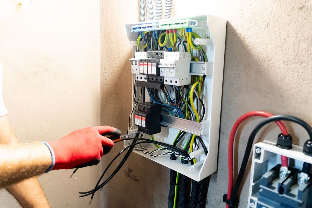 Hand testing wires in an open electrical control panel with colorful cables and breakers