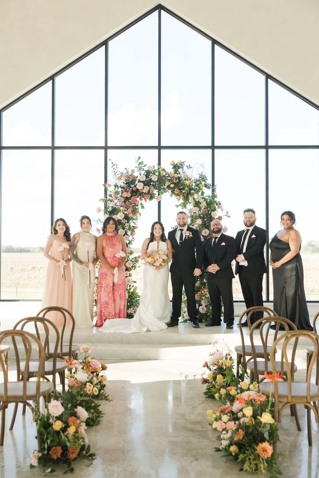 Wedding party posing at the altar in a bright chapel with floral arch and aisle arrangements