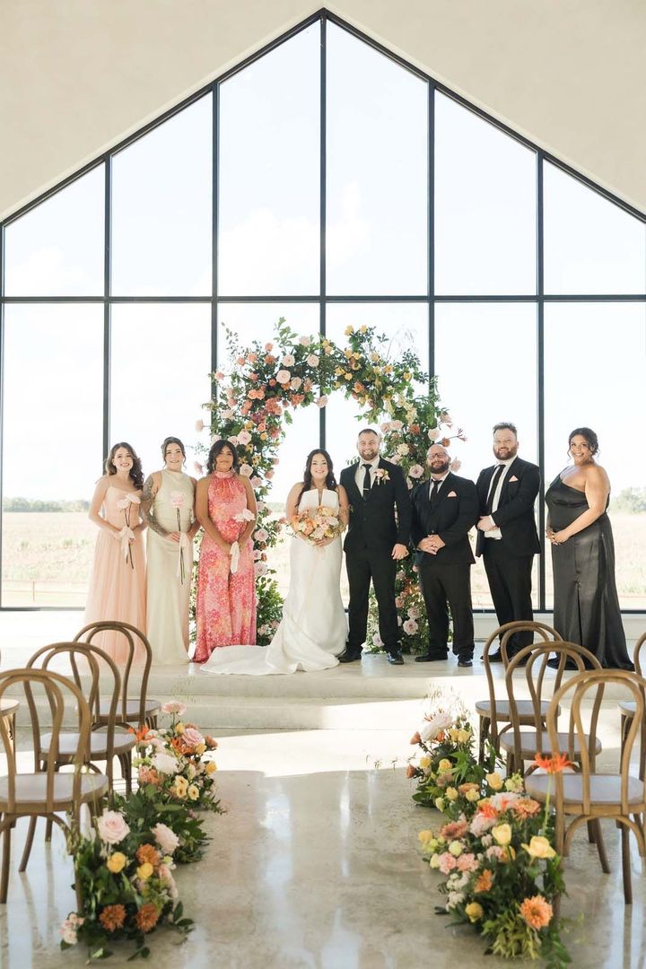 Wedding party posing at the altar in a bright chapel with floral arch and aisle arrangements