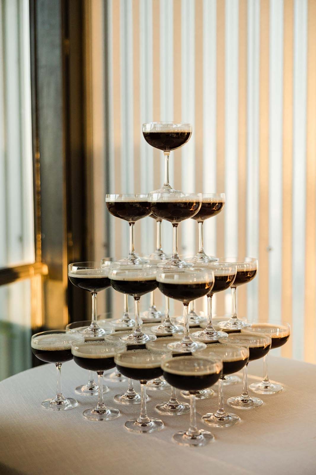 Tower of champagne coupes filled with red wine on a white table, set by a window with striped curtains