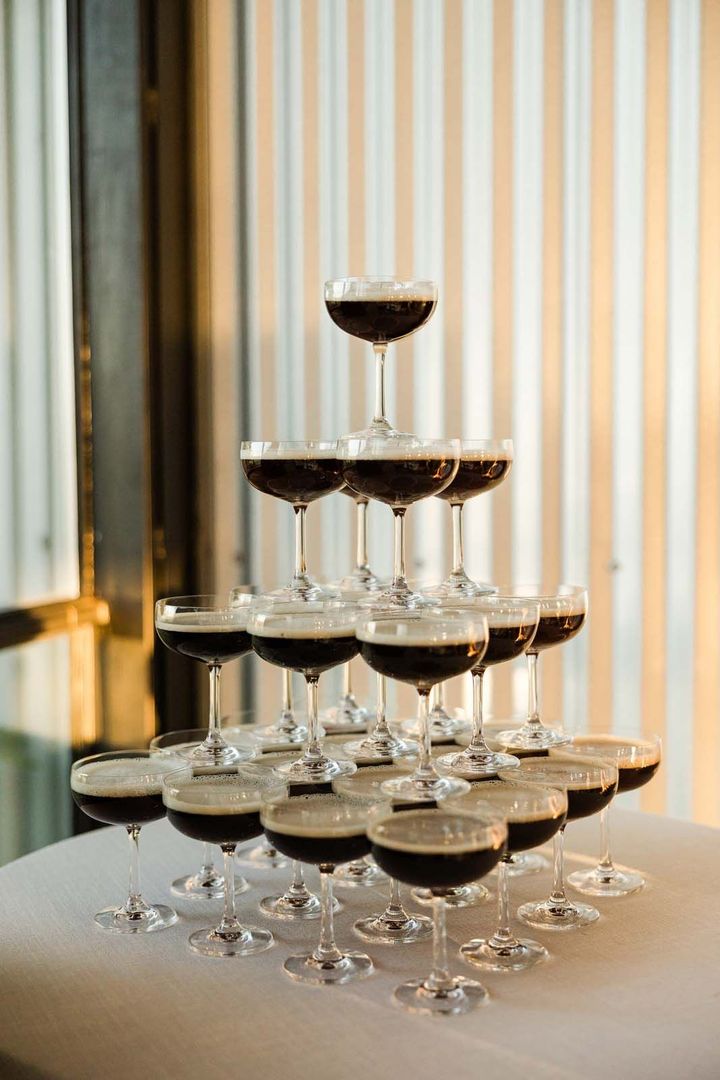 Tower of champagne coupes filled with red wine on a white table, set by a window with striped curtains
