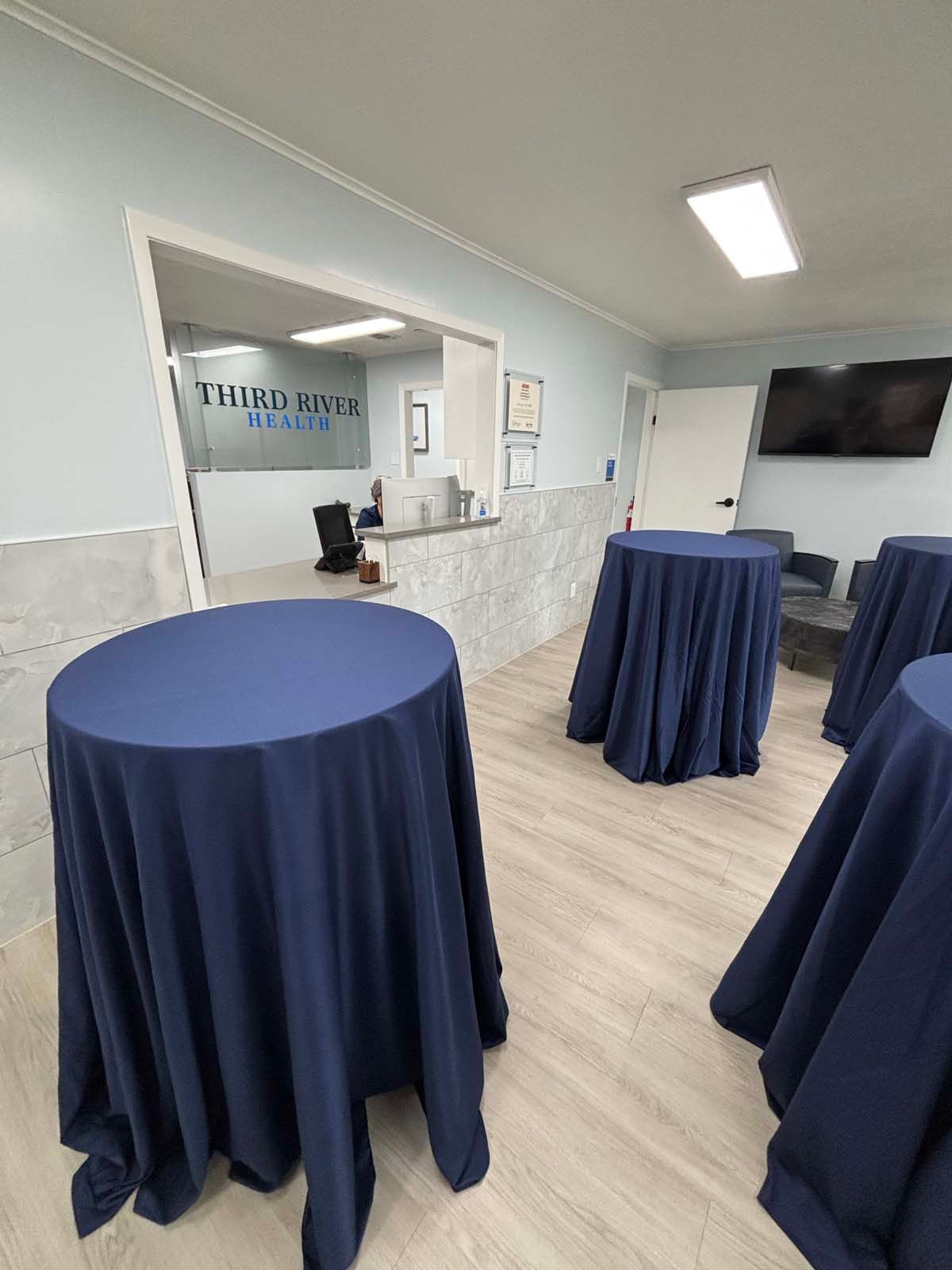 Event room with navy cocktail tables, a reception counter, and a wall-mounted TV