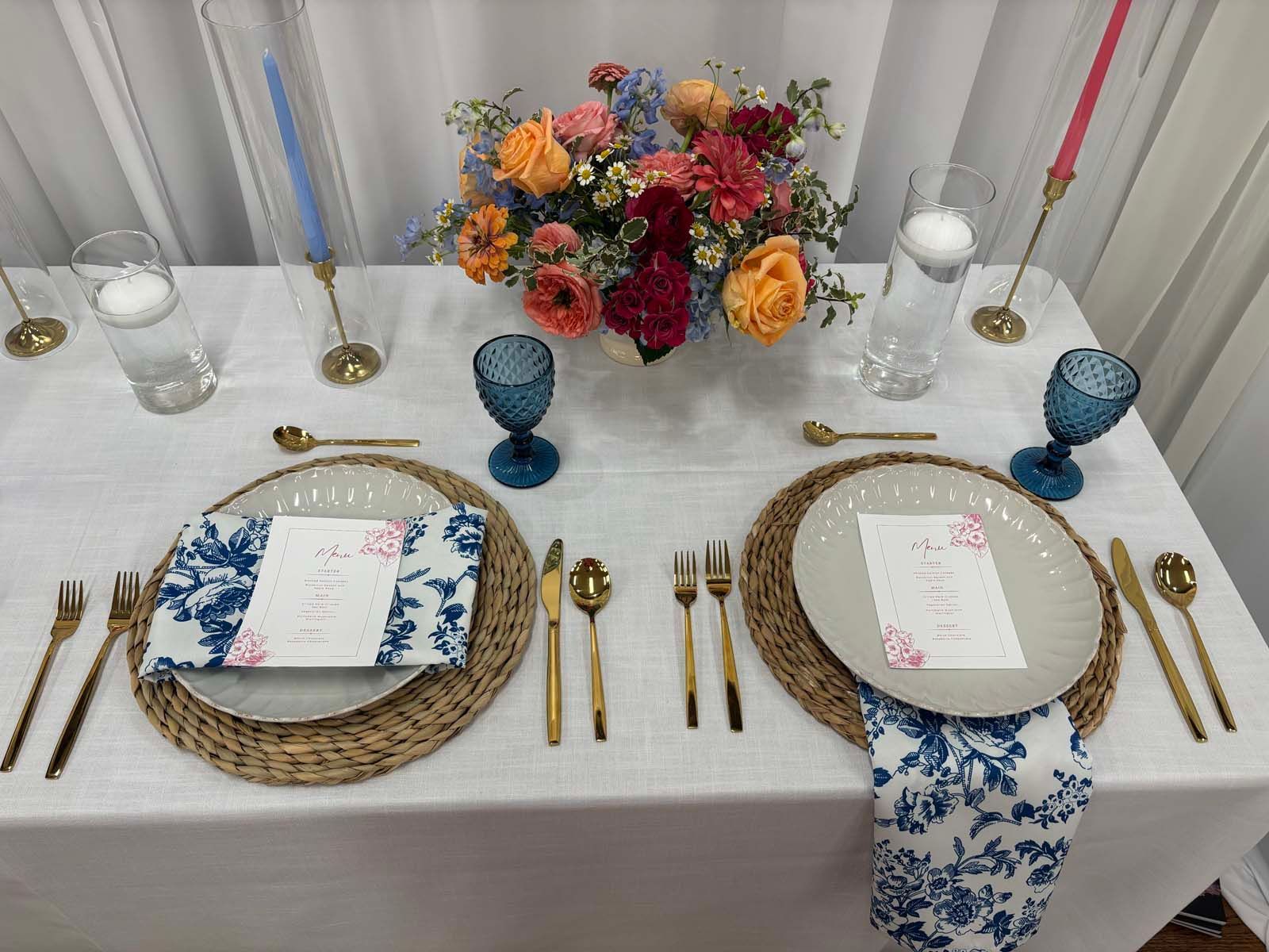 Elegant white table setting with woven chargers, blue accents, and a colorful floral centerpiece