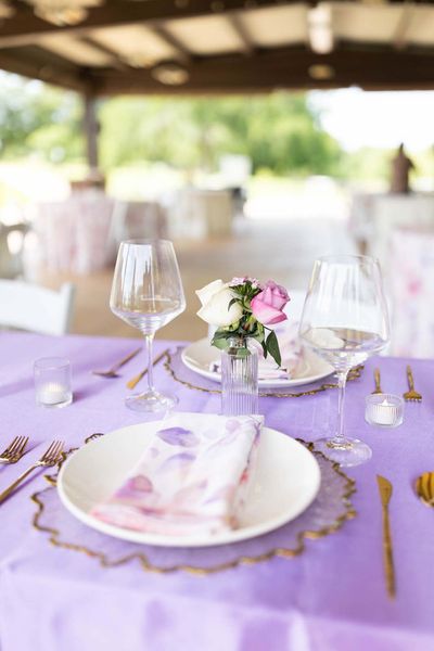 Lavender table setting with floral centerpiece, wine glasses, and gold cutlery at an outdoor reception