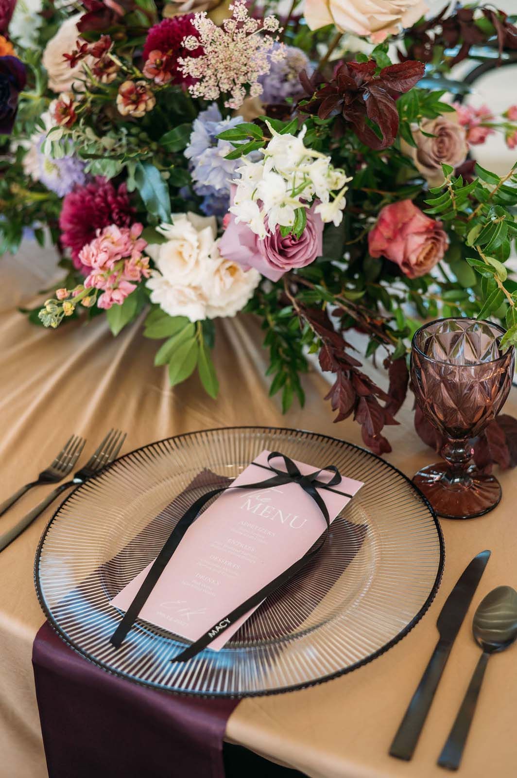 Elegant table setting with floral centerpiece, pink napkin on plate, and dark cutlery on a gold tablecloth