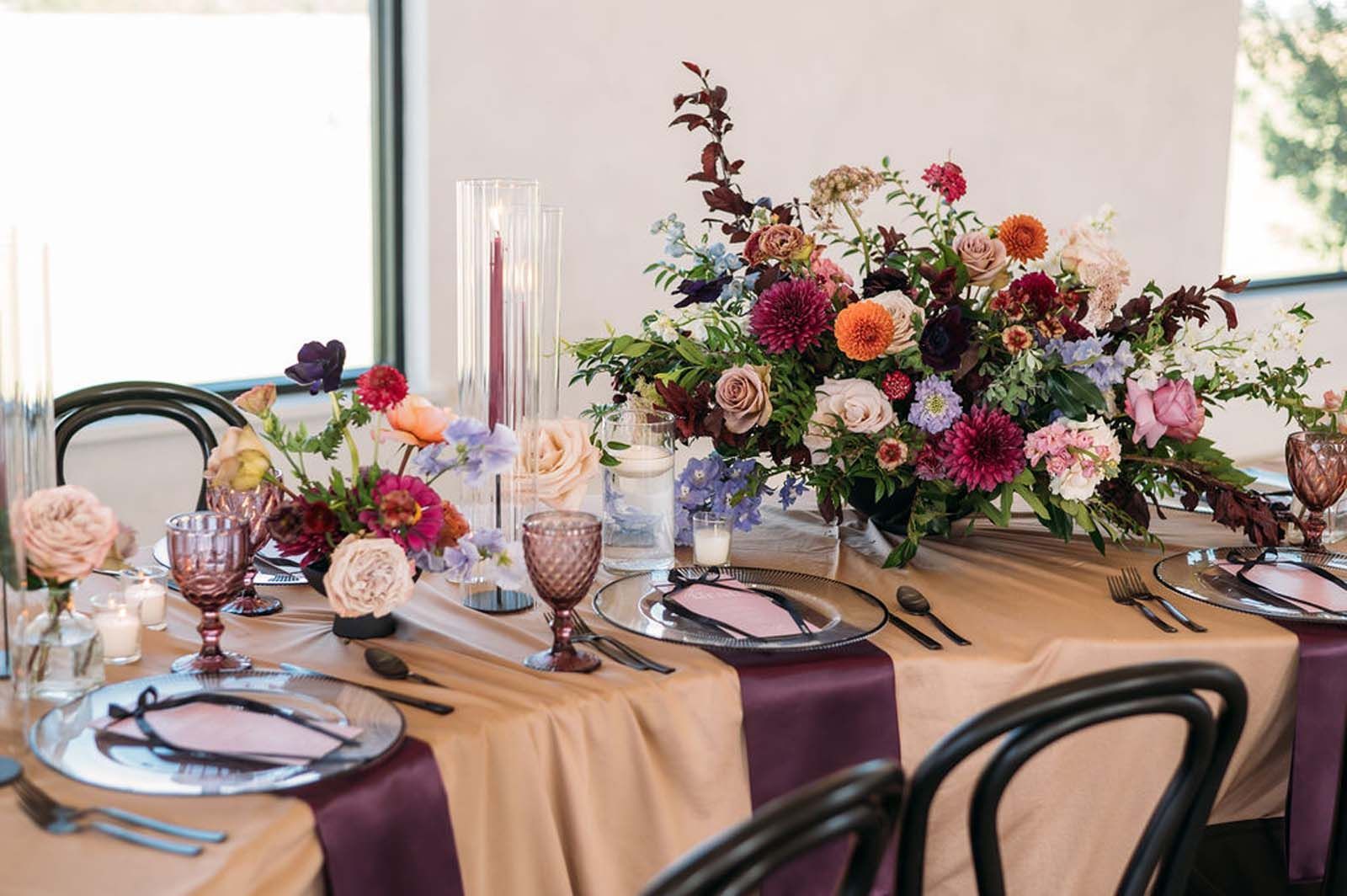 Elegant table setting with floral centerpiece, pink and purple accents, and lit candles by a window