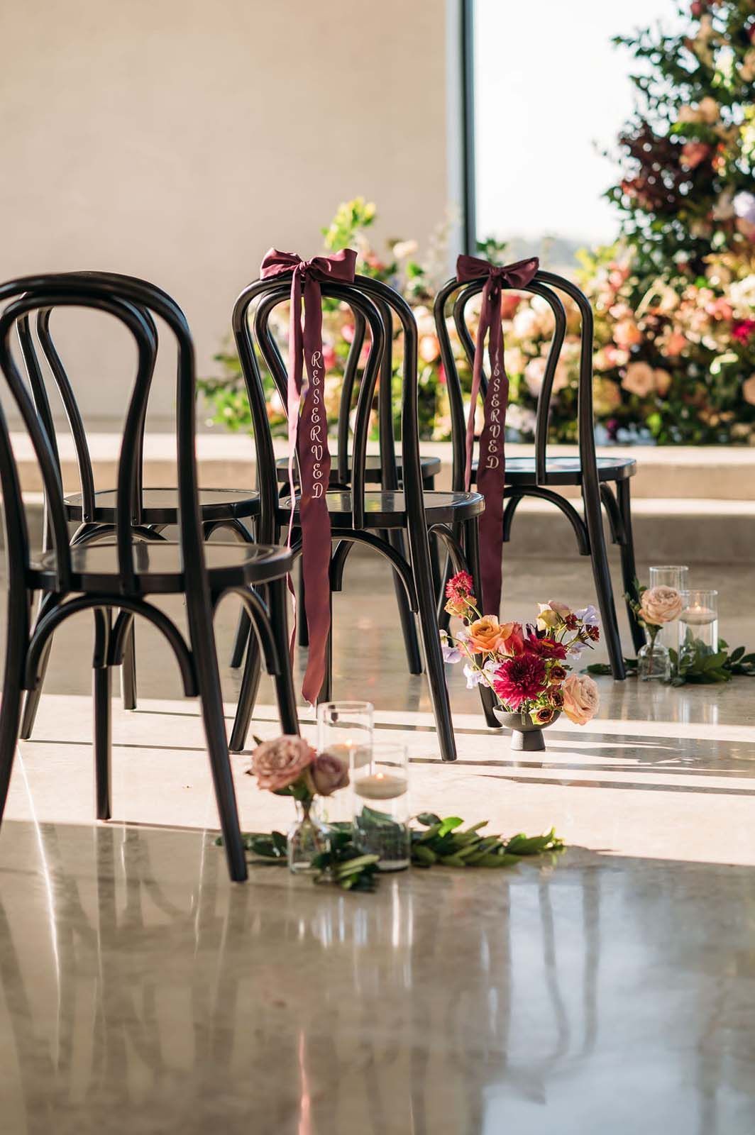 Black chairs with floral decorations on a sunlit polished floor at a wedding venue