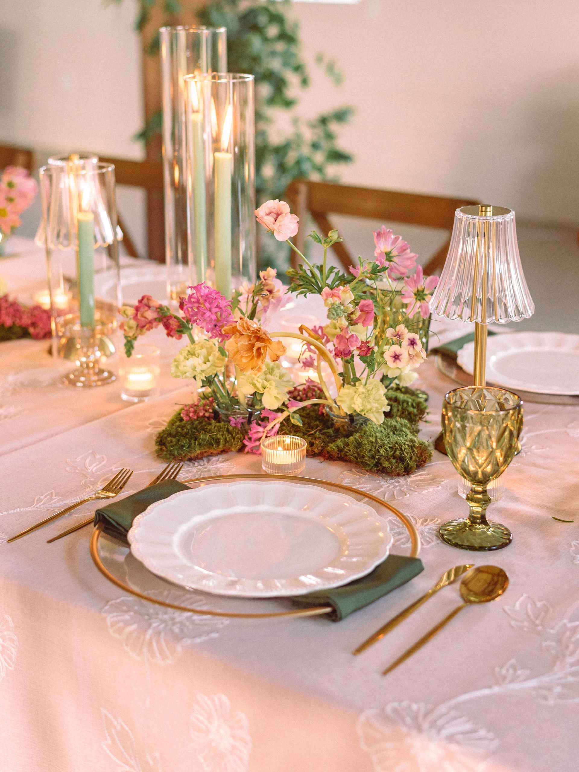 Elegant pink-and-gold tablescape with candles, flowers, and place settings on a softly lit dining table