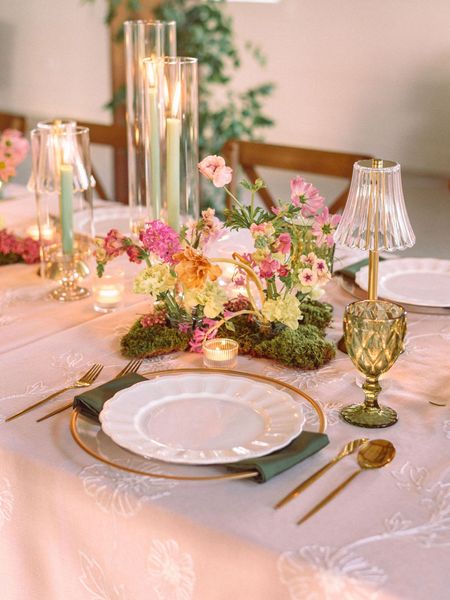 Elegant pink-and-gold tablescape with candles, flowers, and place settings on a softly lit dining table