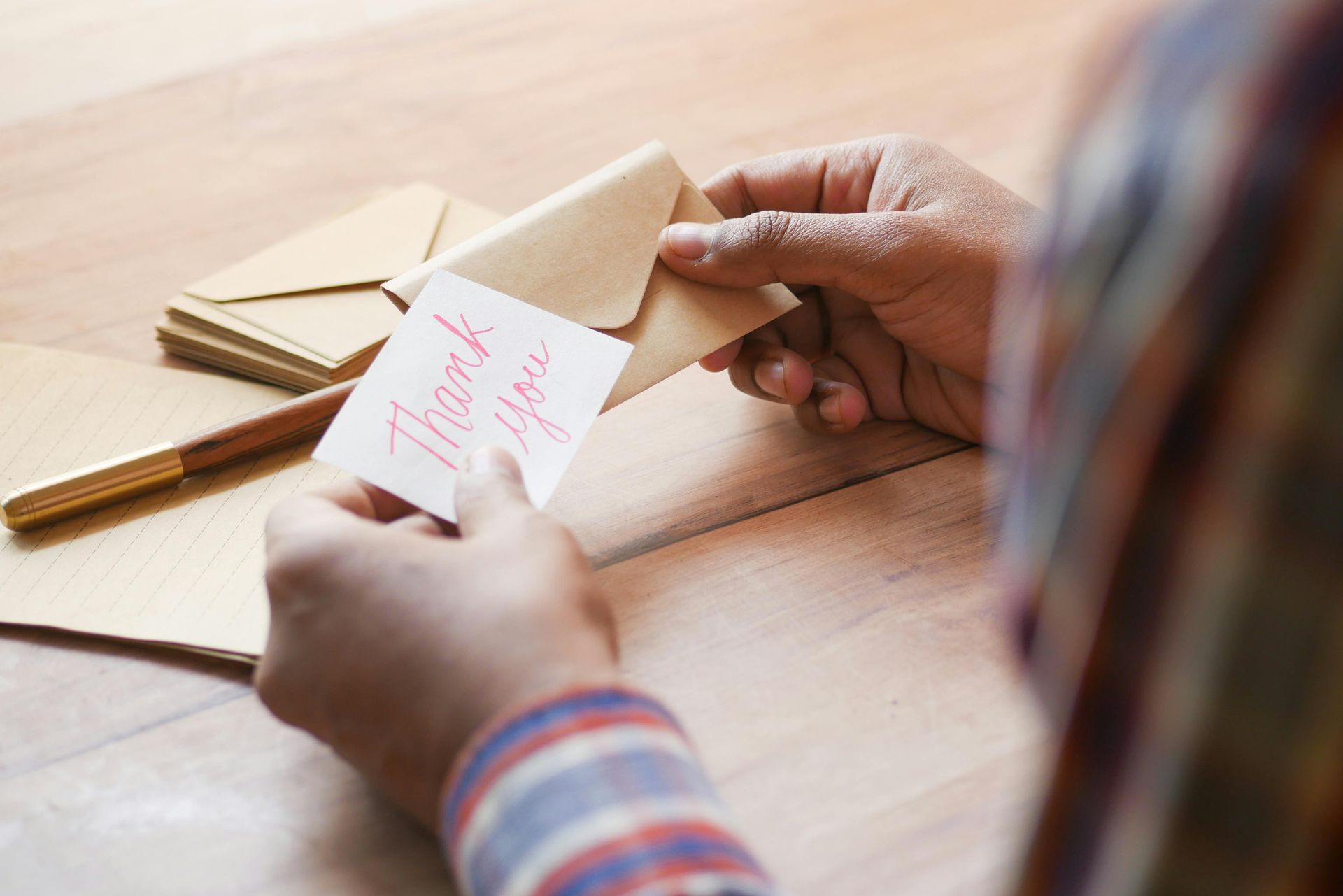 Hands holding a "Thank you" card and envelope on a wooden table.