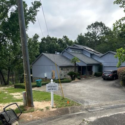 A blue house with a stone facade sits at the end of a driveway, near a utility pole and a real estate sign.