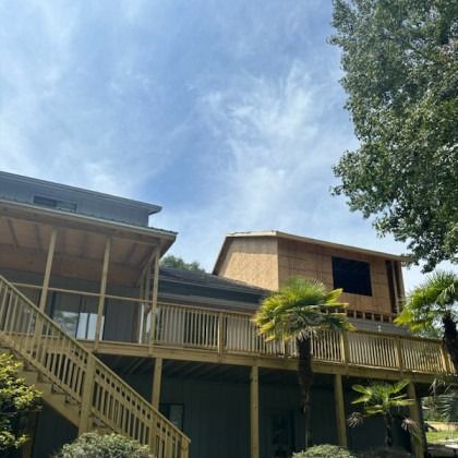 A multi-story house with a wooden deck and staircase under a blue sky, featuring a second-story room under construction.