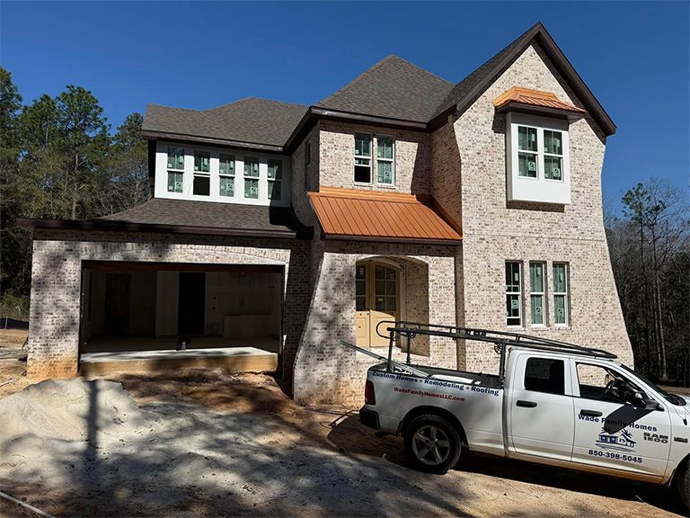 A two-story, light-colored brick house under construction with a white work truck parked in front.