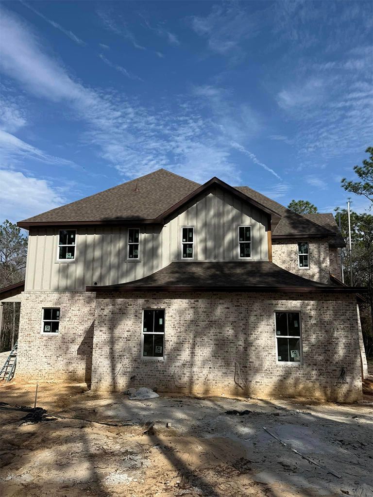 A two-story house under construction with a stone facade on the first floor, vertical siding on the second, and a roof.