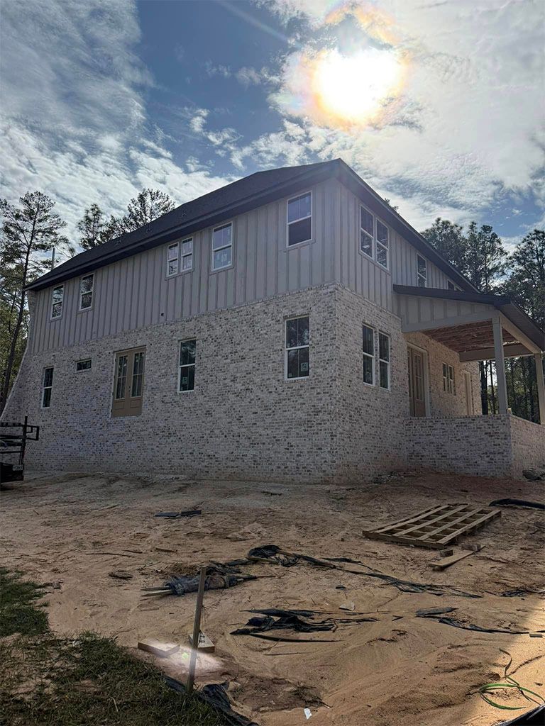 A two-story house under construction with white brick on the lower level and light gray vertical siding on the upper level.