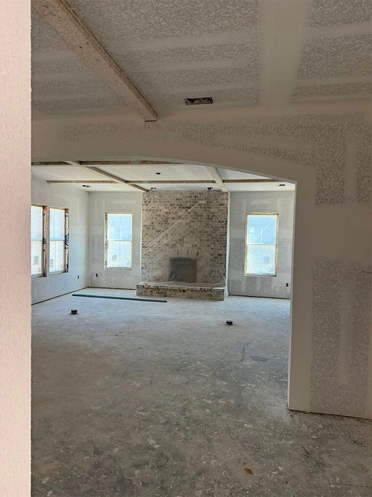 An interior view of a room under construction, featuring an arched entryway, drywall, and a central stone fireplace.