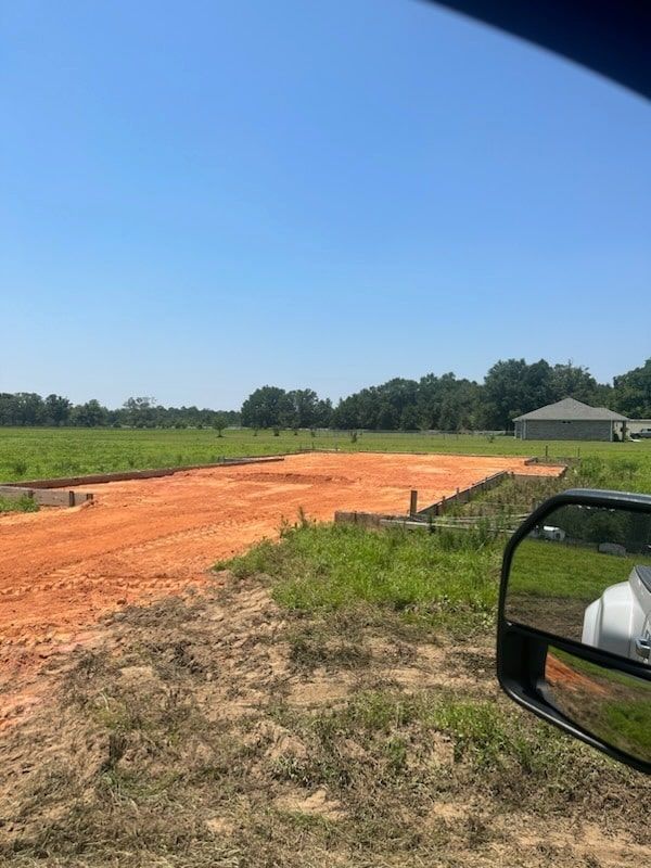 A rectangular plot of land prepared for construction with orange clay, bordered by wooden forms under a clear blue sky.