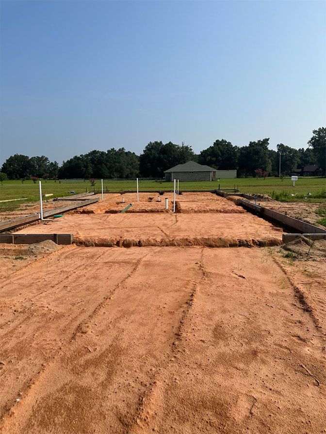A construction site with a red dirt foundation and concrete footings prepared for a new house under a clear blue sky.