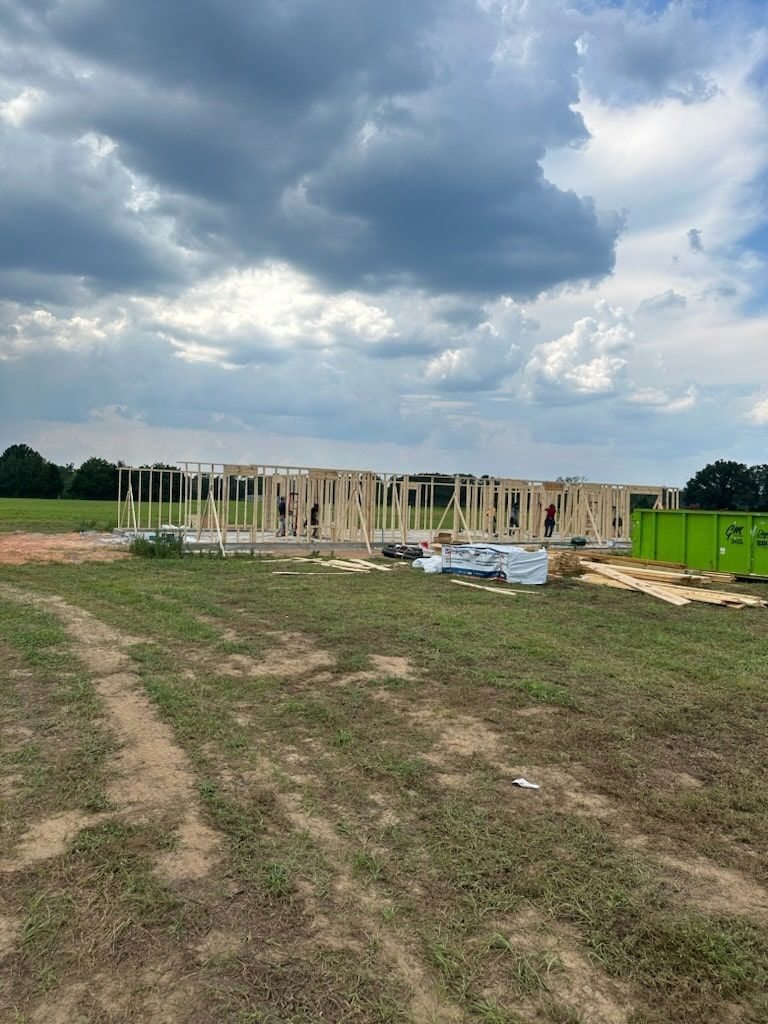 Construction site with a wooden wall frame in a rural field under a cloudy, dramatic sky.