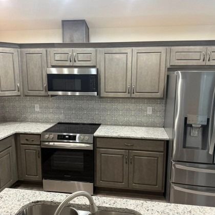 A modern kitchen with grey cabinets, stainless steel appliances, and light-colored speckled granite countertops.