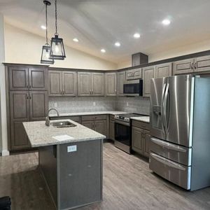 A modern kitchen with grey cabinets, granite countertops, a central island, and stainless steel appliances.