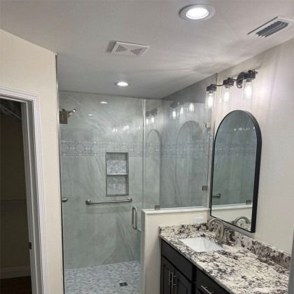 Modern bathroom featuring a walk-in glass shower with marble-look tile, next to a vanity with a granite countertop.