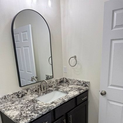 A modern bathroom vanity with a marbled countertop, dark cabinet, and arched mirror on a white wall.
