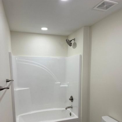 A white fiberglass bathtub and shower surround with brushed nickel fixtures in a neutrally painted bathroom.