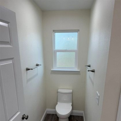 A small, neutral-toned half-bathroom featuring a white toilet, a frosted window, and two silver towel bars on side walls.