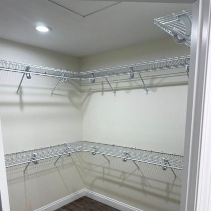 An empty walk-in closet featuring two levels of white wire shelving mounted on light-colored walls.