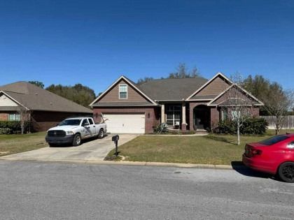 A suburban brick house with a two-car garage, a white pickup truck in the driveway, and a red car parked on the street.