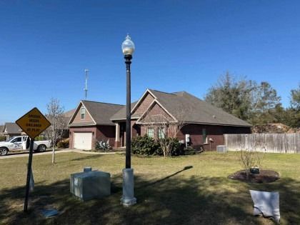 A brick house with a dark shingle roof stands under a clear blue sky, featuring a street lamp and caution sign in the yard.