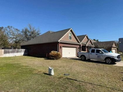 A tan and brick suburban house with a white garage door and a white work truck parked in the driveway on a sunny day.