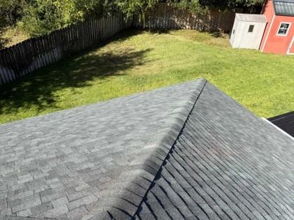 High-angle view of a grey shingled roof overlooking a green backyard with a wooden fence and a small red shed.