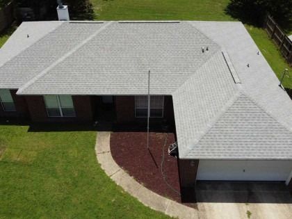 Aerial view of a single-story brick house with a gray shingled roof, a front lawn, and a paved driveway.