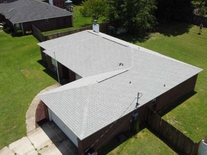 Aerial view of a residential house with a light gray shingled roof, a brick exterior, and a surrounding grass lawn.