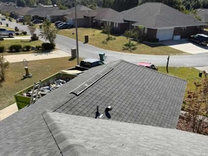 An elevated view of a residential shingle roof with a ridge vent, overlooking a suburban street with parked cars.