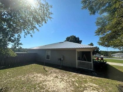 A gray house with a metal roof and a screened-in porch sits in a sunny yard under a bright blue sky.