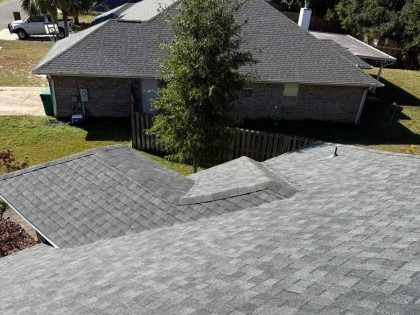 A high-angle view of gray asphalt shingled roofs on two residential houses with a green tree between them.