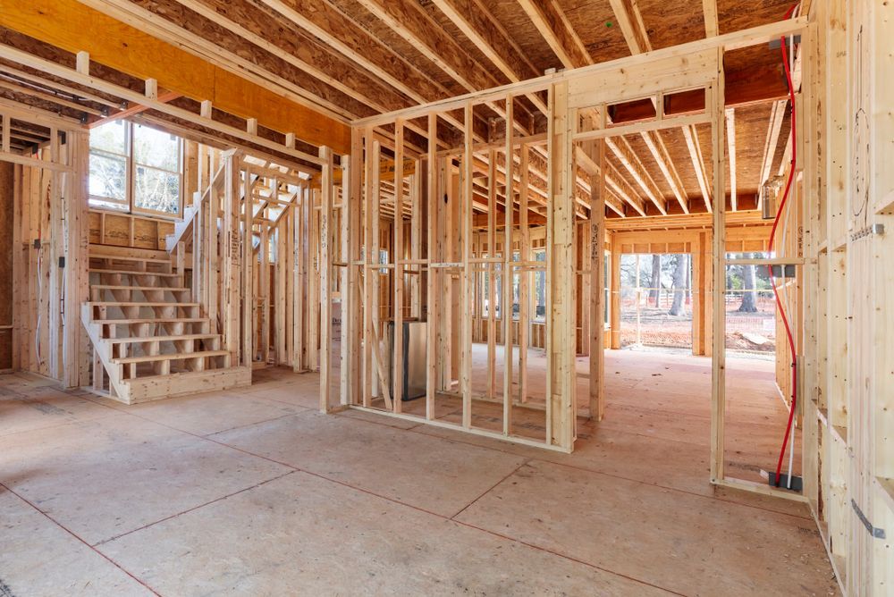 Interior view of a residential building under construction, featuring wooden wall studs, floor joists, and a staircase.