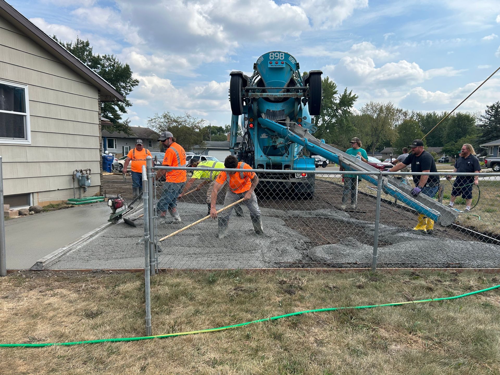 A group of construction workers are working on a concrete driveway in front of a house.