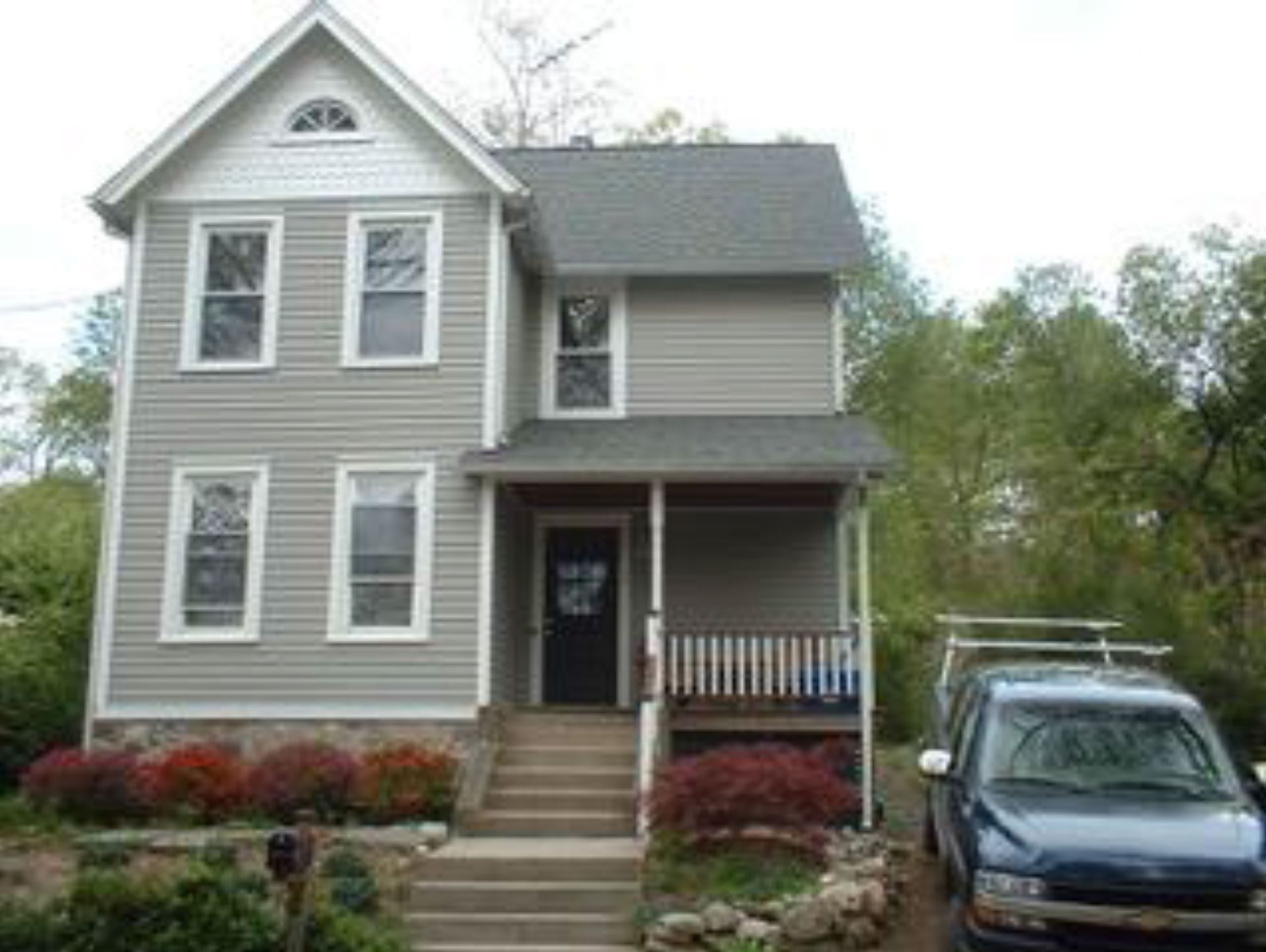 Two-story house with gray siding, front porch, and blue SUV parked in driveway.