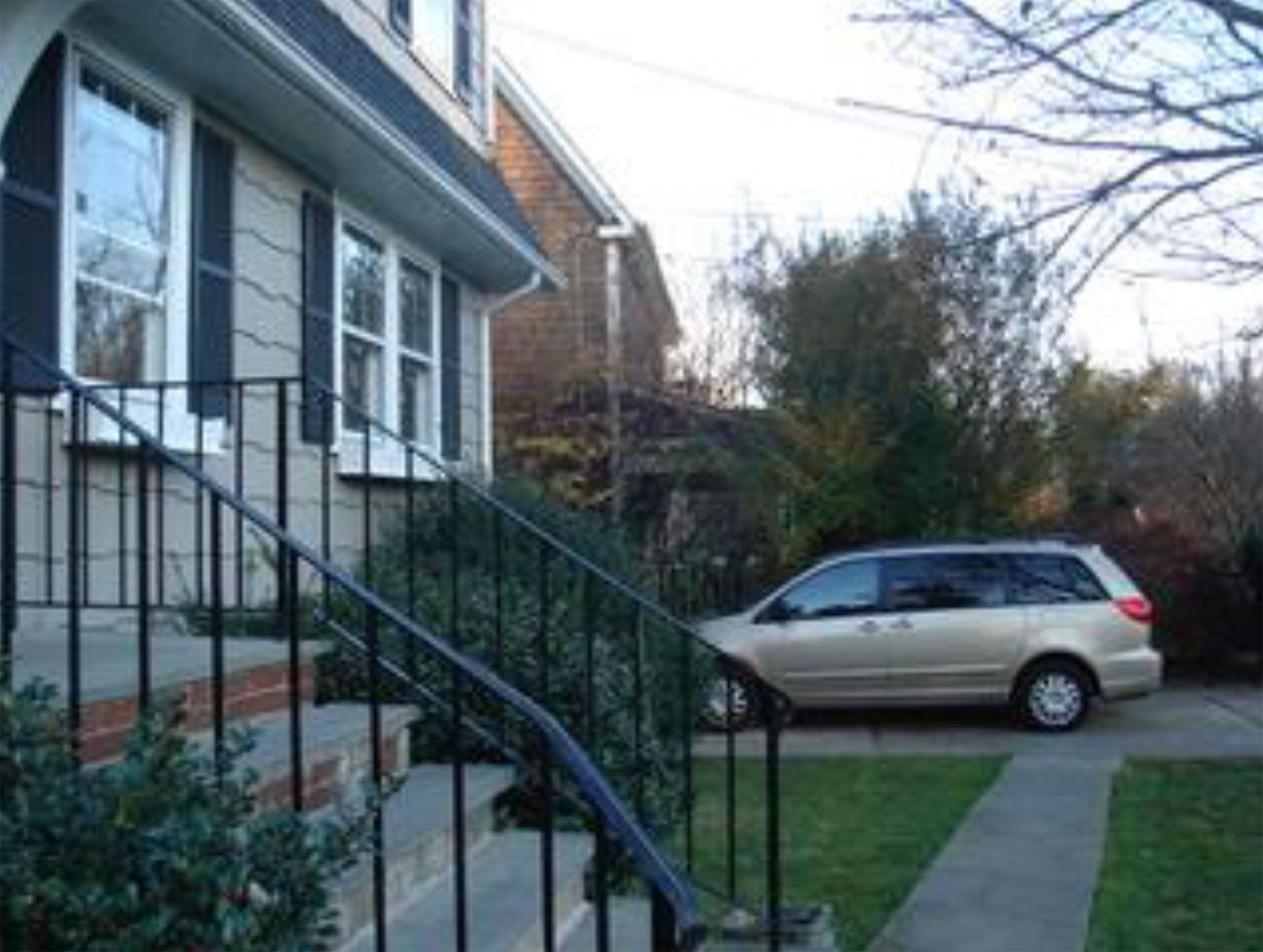 House with black railing, beige minivan parked in the driveway, and a small patch of lawn.