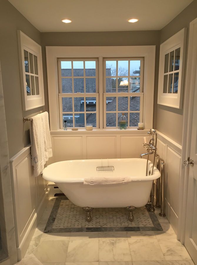 Bathroom with a claw-foot tub under a window, flanked by two small windows and wainscoting.