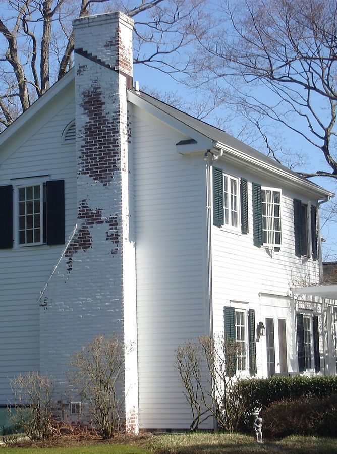 White house with green shutters and a brick chimney, partially exposed.
