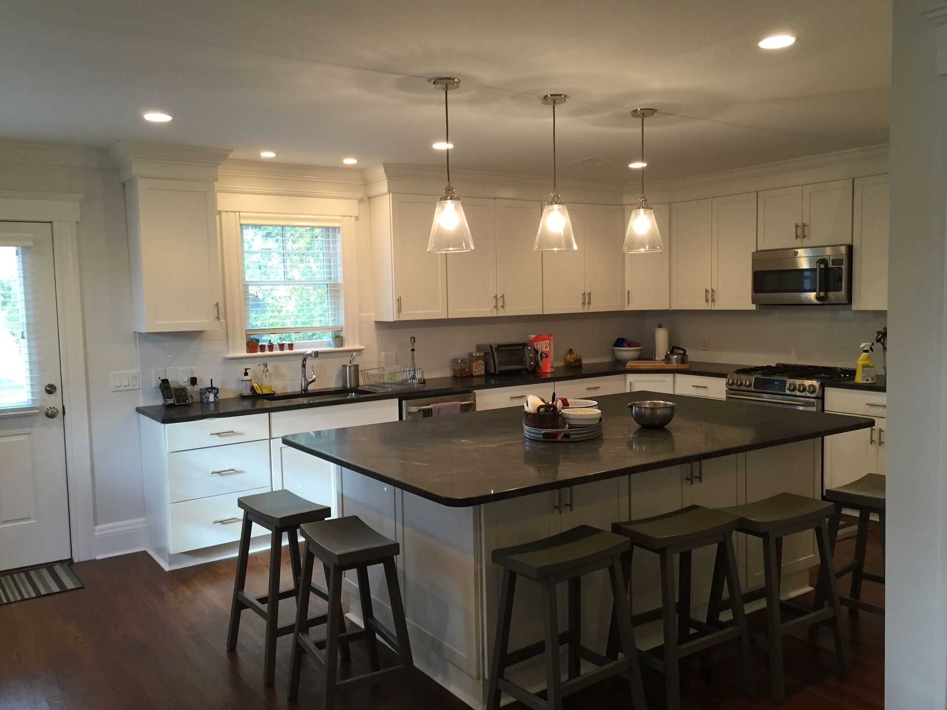 Custom Kitchen Remodeling White kitchen with island, gray countertops, and bar stools.