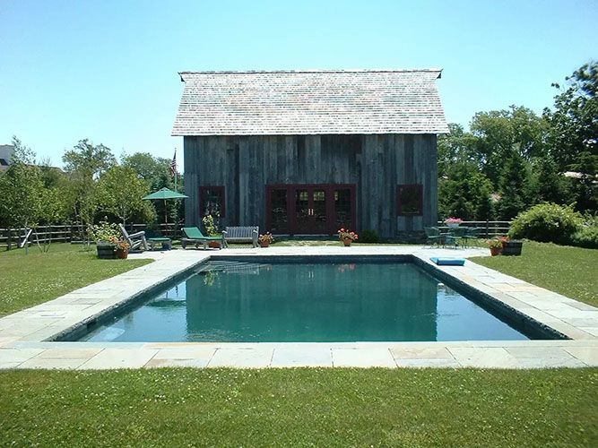Backyard with a pool in front of a weathered barn under a clear blue sky.